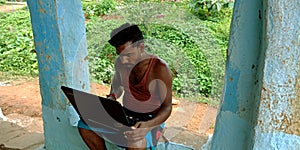 An indian village poor man operating laptop computer system seating at corridor