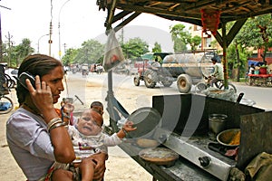 Indian woman with baby talking on her mobile phone at a roadside eatery place.