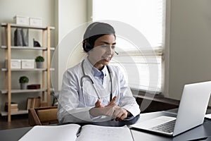 Indian woman doctor in wireless headphones talking, using laptop