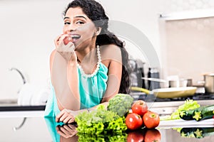 Indian woman eating healthy apple in her kitchen