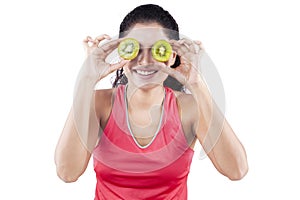 Indian woman holding kiwi fruit on her eyes