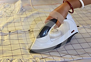 Indian woman ironing clothes using iron on floor after laundry at home. Making household working at home. Laundry service and maid