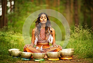 Indian Woman meditating with Tibetan Singing Bowls Outdoors. Yoga Practice in Forest. Spiritual Sound Healing Therapy. Peaceful