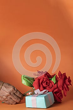 Indian woman\'s hand holding a red roses bouquet with Gift box on orange background. Valentine\'s day concept