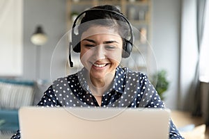 Indian woman wear headset looks at laptop talk by videocall