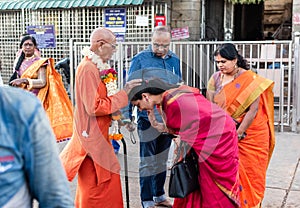 An Indian woman wearing a traditional sari taking the blessings of a monk in a saffron