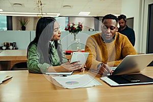 Indian woman working off digital tablet discussing work with mixed race man typing on laptop in office