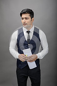 Indian young business man giving presentation on a topic holding folder in hand in formal wear wearing white shirt, black tie,