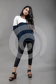 Indian young female model in casual winterwear against grey background. Long black haired model wearing black leggings, blue and