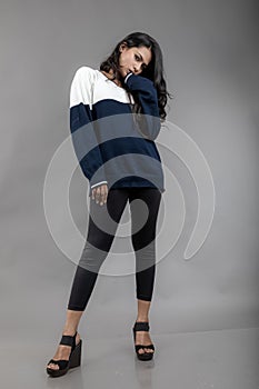 Indian young female model in casual winterwear against grey background. Long black haired model wearing black leggings, blue and