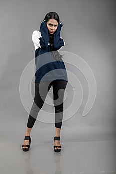 Indian young female model in casual winterwear against grey background. Long black haired model wearing black leggings, blue and