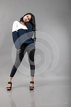 Indian young female model in casual winterwear against grey background. Long black haired model wearing black leggings, blue and