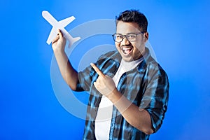 Indian young man holding paper cutting airplane and pointing with finger