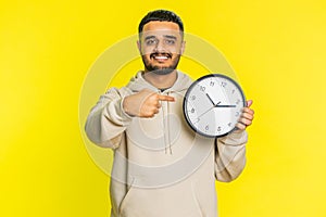 Indian young man showing time hour on wall office clock, ok, thumb up, approve, hurry up, deadline