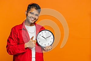 Indian young man showing time hour on wall office clock, ok, thumb up, approve, hurry up, deadline