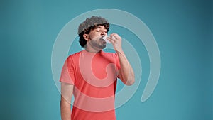 indian young man sneezes or coughs and wipes himself with a tissue against a blue studio background