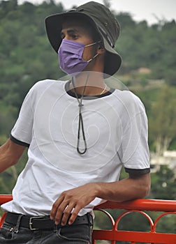 A Indian young man standing outside with wearing boonie hat, white t-shirt and face mask during coronavirus pandemic with looking