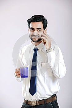 Indian young man talking on cellphone and holding cup in hand