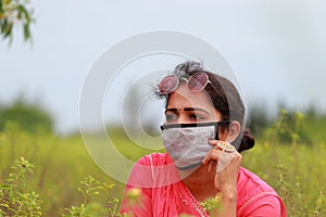 An Indian young stylish female model posing in a field wearing a brown face mask to prevent corona disease