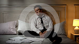 Indifferent businessman sitting around documents on bed, desire to change work