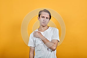 Indifferent man in white t-shirt on yellow background looks forward head bent