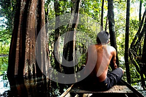 Indigenous man riding a canoe into the wet forest in Brazil