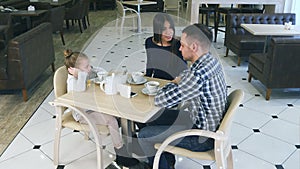 Indignant mother blaming on daughter and husband in cafe. Littke girl closing her ears.