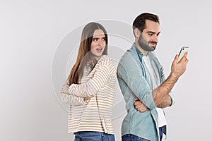 Indignant woman looking into boyfriend`s smartphone on light grey background. Relationship problems