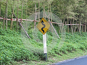 Inding road sign,yellow winding road ahead sign in pine wood mountain street