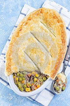 Individual beef pot pie or deep dish pie in baking dish, crust broken open, vertical, top view