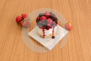 Individual cheesecake with all kinds of red berries and jam on a gray marble plate