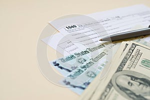 1040 Individual Income tax return form with Refund Check and hundred dollar bills on beige background