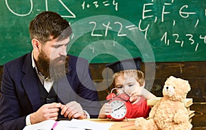 Individual lesson concept. Boy, child on calm face holds alarm clock while teacher talk to kid. Teacher with beard