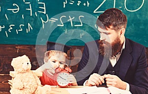 Individual lesson concept. Boy, child on calm face holds alarm clock while teacher talk to kid. Teacher with beard