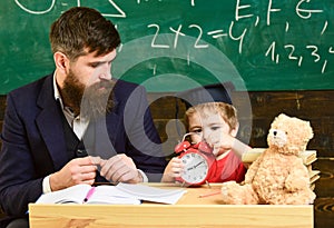 Individual lesson concept. Teacher with beard, father teaches little son in classroom, chalkboard on background. Boy