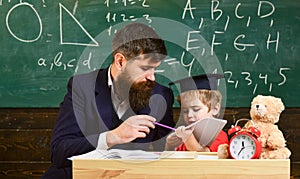 Individual schooling concept. Teacher and pupil in mortarboard, chalkboard on background. Kid studies individually with