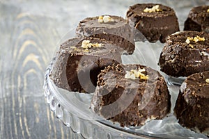 Individual small baked chocolate and walnut pudding cake, brown in color, on display on a glass plate put on a rustic wooden table