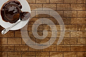 An individual sticky toffee sponge cake, with a sticky toffee sauce, on a white plate with a spoon, on a checked wooden surface