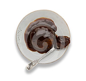 An individual sticky toffee sponge cake, with a sticky toffee sauce, on a white plate with a spoon, isolated on white