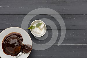 An individual sticky toffee sponge cake, with a sticky toffee sauce, on a white plate with a spoon, and a small bowl of ice cream