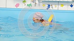 Individual swimming lesson with a male personal trainer in an indoor pool. Happy preschool girl is learning to swim with