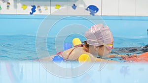 Individual swimming lesson with a male personal trainer in an indoor pool. Happy preschool girl is learning to swim with