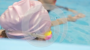 Individual swimming lesson with a male personal trainer in an indoor pool. Happy preschool girl is learning to swim with