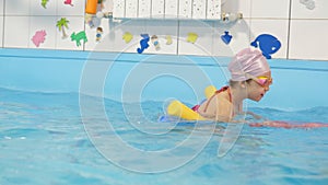 Individual swimming lesson with a male personal trainer in an indoor pool. Happy preschool girl is learning to swim with