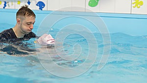 Individual swimming lesson with a male personal trainer in an indoor pool. Happy preschool girl is learning to swim with