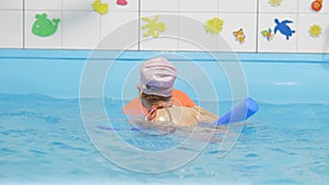 Individual swimming lesson with a personal trainer in an indoor pool. Happy preschool girl is learning to swim with pool