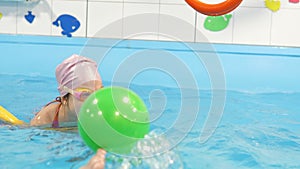 Individual swimming lesson with trainer in an indoor pool. Happy preschool girl is learning to swim with pool noodle in