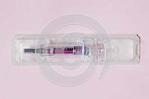 Individually sealed syringe pre-filled with a medical solution in a plastic blister on a textured pink paper background.