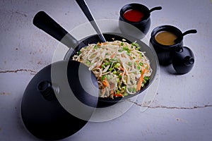 Indo-Chinese dish of fried noodles and vegetables in a fryingpan served with sauces in little bowls