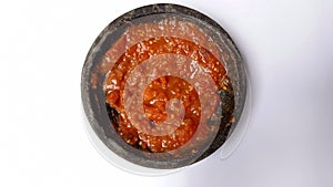 Indonesian chilli sauce is called sambal, delicious sambal terasi grind in a traditional mortal stone on a white background